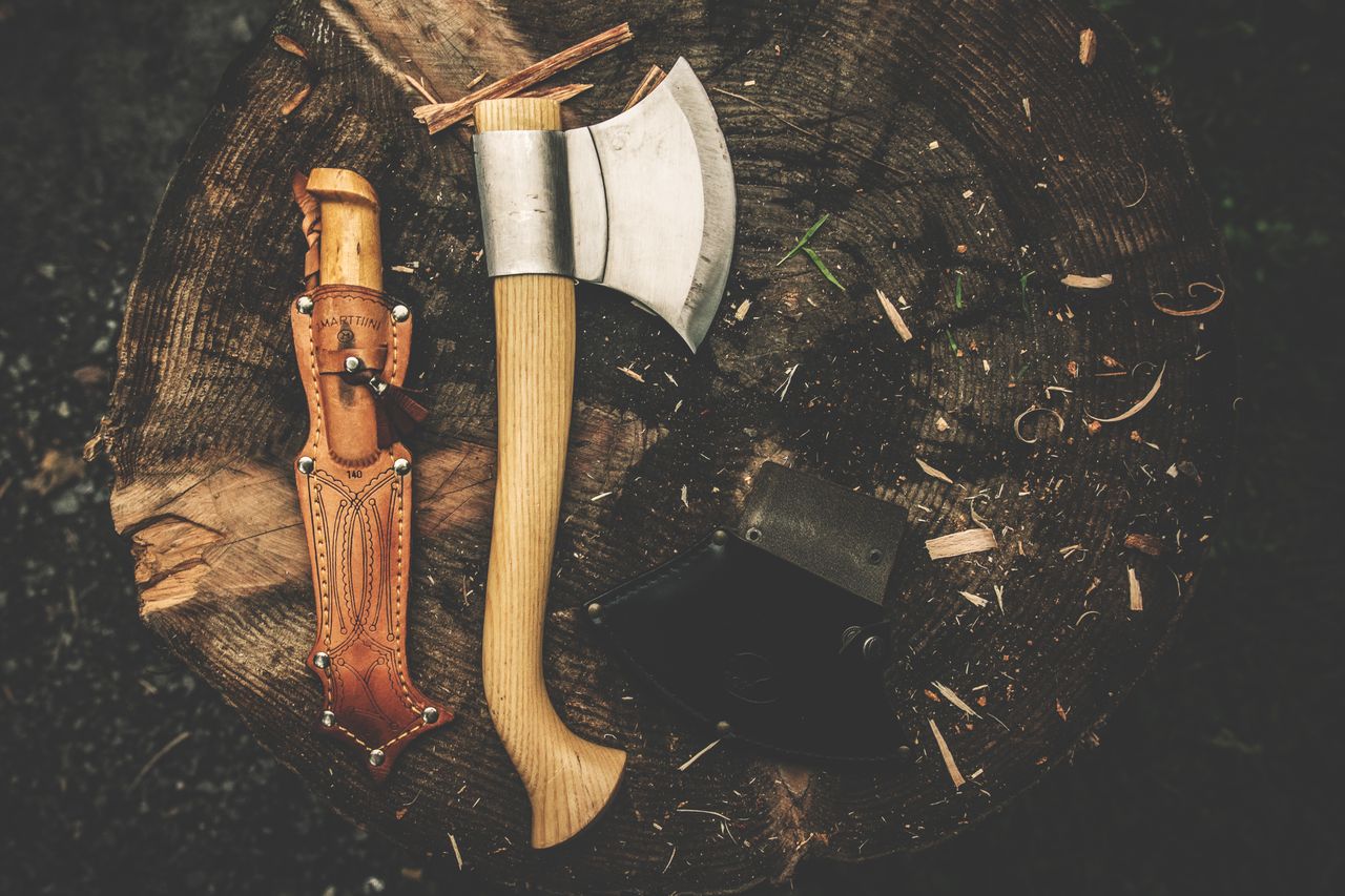 A rugged camping axe and knife on a tree stump, perfect for bushcraft and outdoor adventures.