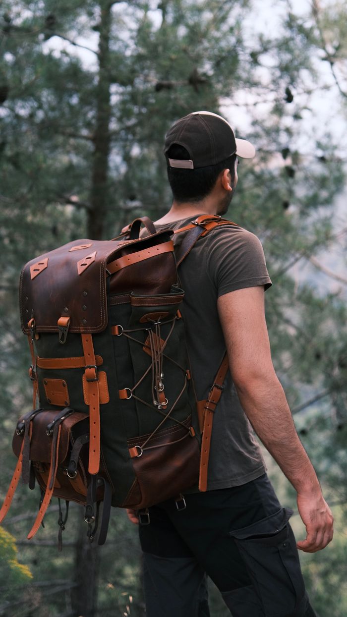A man with a leather backpack stands in a forest, capturing the essence of adventure.