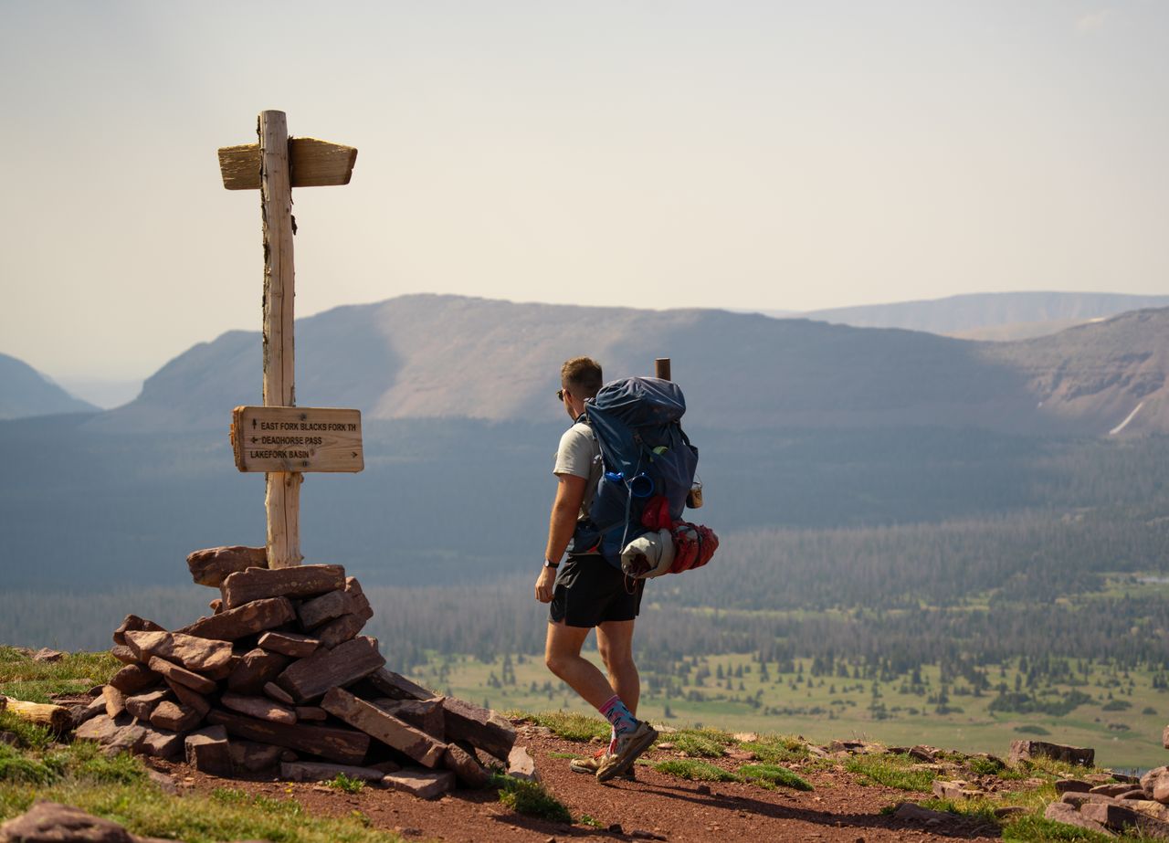 A man hiking with a backpack past a trail sign in the Uinta Mountains, Utah.