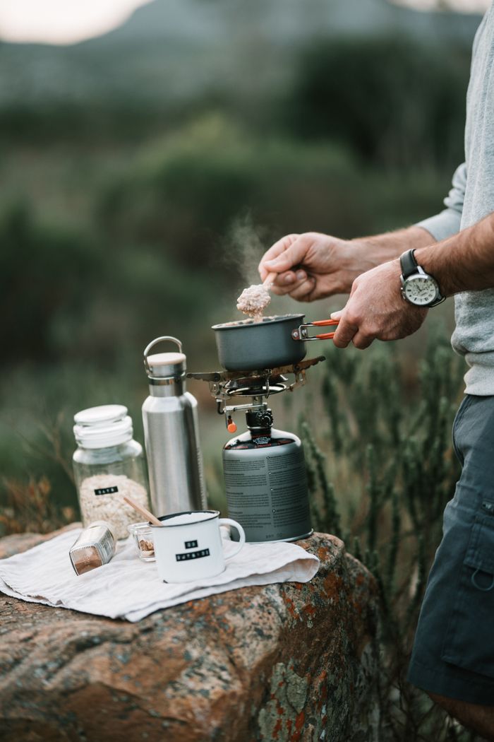 Person cooking oatmeal outdoors with a portable stove on a camping trip.
